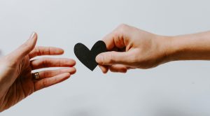 Hand giving a paper heart to another