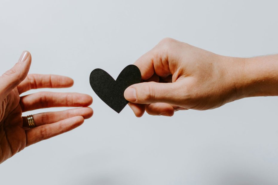 Hand giving a paper heart to another