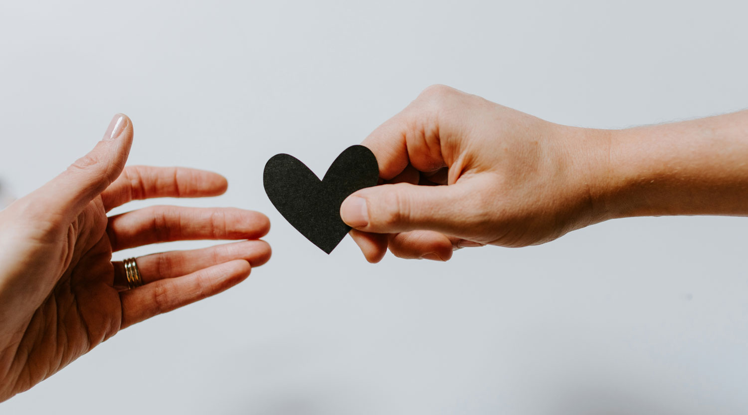 Hand giving a paper heart to another